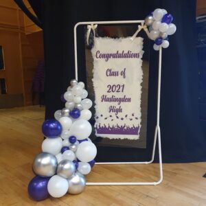 A decorative display featuring a banner that says 'Congratulations Class of 2021 Haslingden High', surrounded by a cluster of purple, white, and silver balloons.